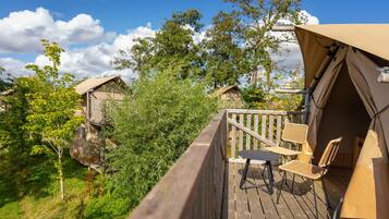 A wooden deck with outdoor furniture, a covered area with a table and chairs, and surrounding greenery.