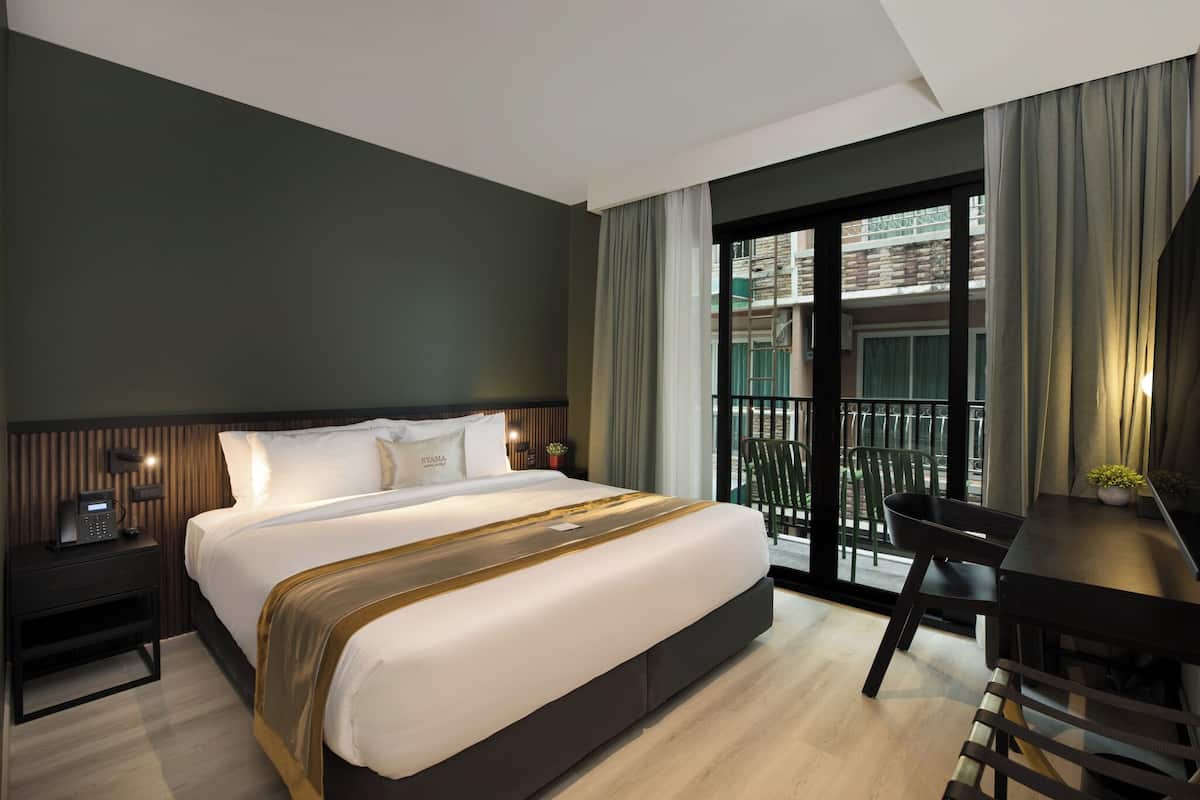 A modern hotel room with a large bed, a desk, and a balcony with a view of the city.