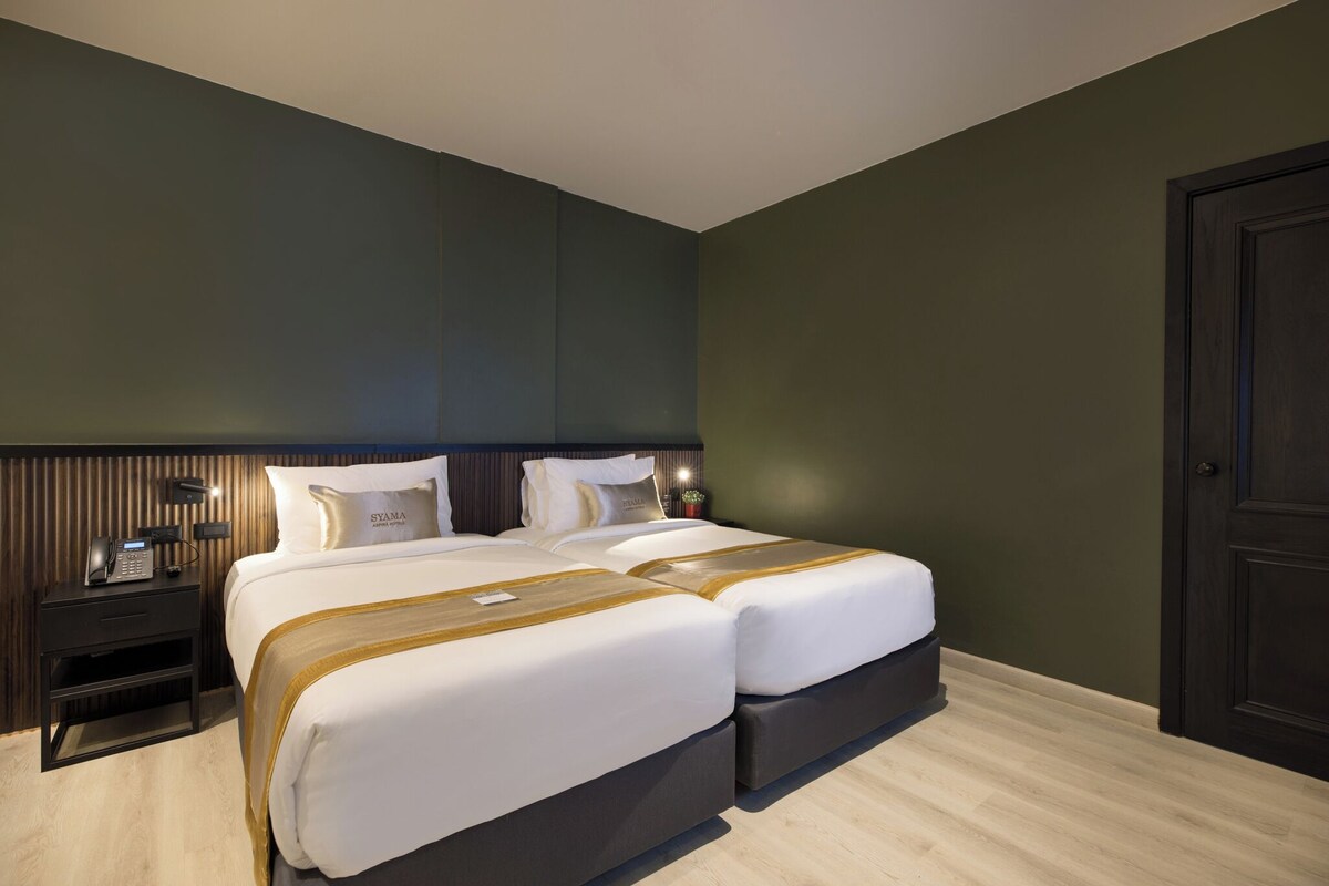 A hotel room with a double bed, a bedside table with a phone, and a dark wooden headboard.
