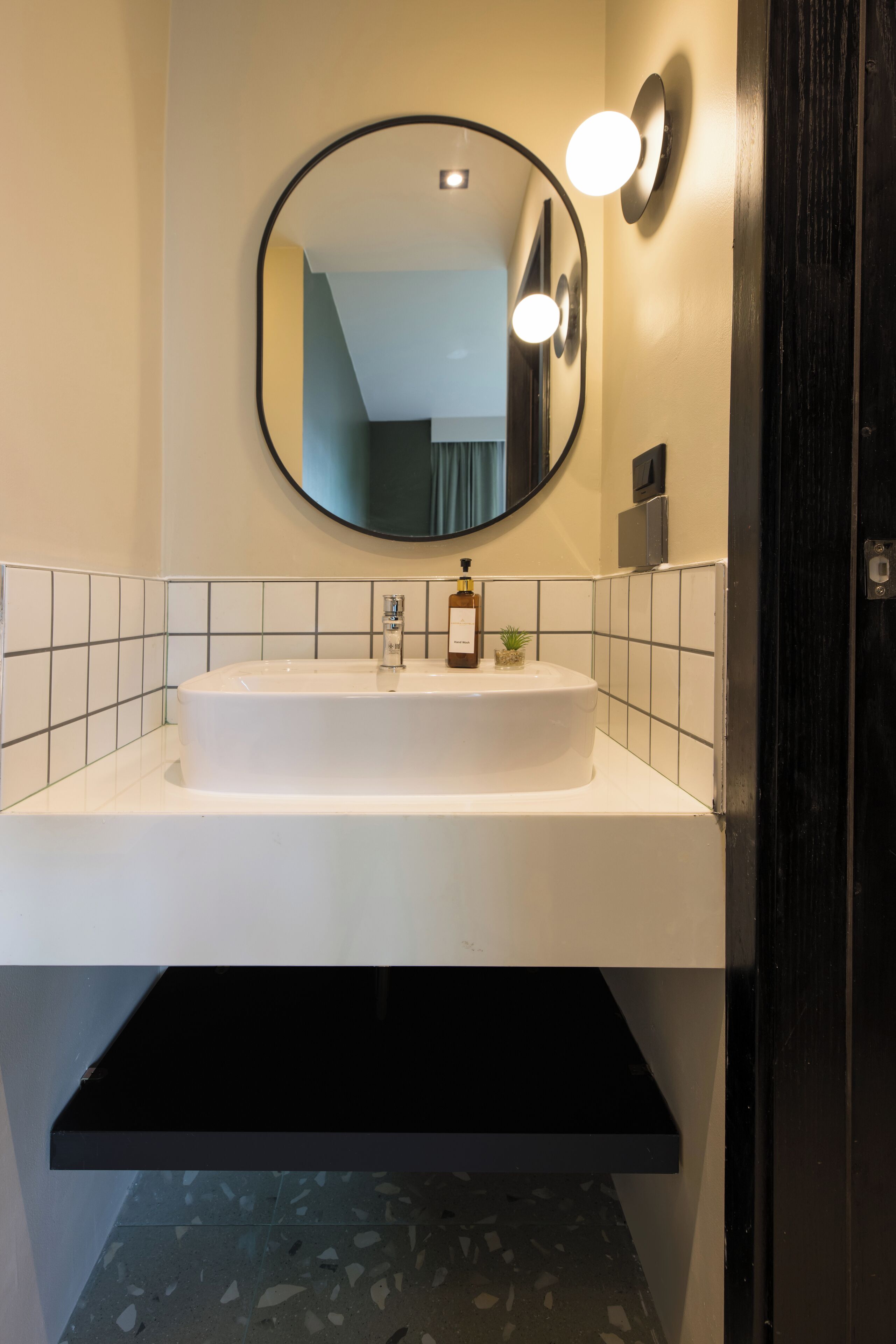 A bathroom with a white sink, a round mirror, and a black shelf below.
