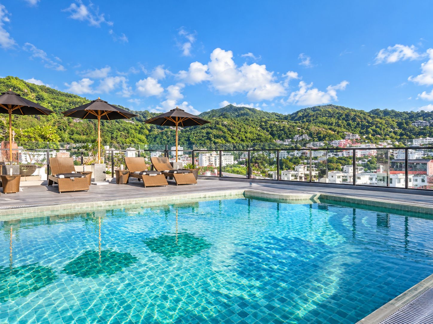 A rooftop pool with lounge chairs and umbrellas, surrounded by a cityscape and hills.