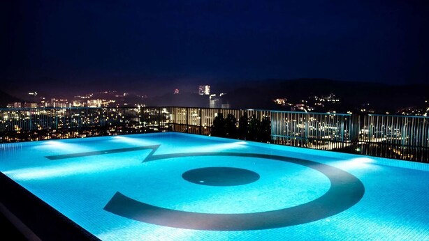 A rooftop pool with a geometric design, surrounded by a railing, overlooking a cityscape at night. - 3 Towers Jln Ampang by Airhost (Kuala Lumpur)