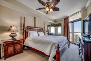 A bedroom with a large bed, wooden headboard, a ceiling fan, a nightstand with a lamp, a dresser, and a large window with a view. - New to Rental! Gorgeous 6th Floor Oceanfront Condo at North Beach Resort-$300 FREE Activities Daily (North Myrtle Beach)
