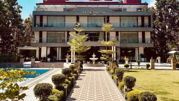 A two-story building with a sign reading "The Greenicon." It features a central courtyard with a fountain, surrounded by neatly trimmed bushes and a tiled walkway. - The Green Icon Resort (Rishikesh)