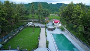 A residential area with a swimming pool, a lawn, and a view of a mountain range. - The Green Icon Resort (Rishikesh)