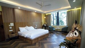 A modern hotel room with a wooden headboard, a large bed, a desk, a chair, and a potted plant. - The Green Icon Resort (Rishikesh)