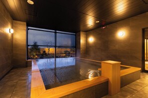 A modern indoor hot tub area with wooden benches and a view of a garden through a wooden partition. - ITSUMU (Oshu)