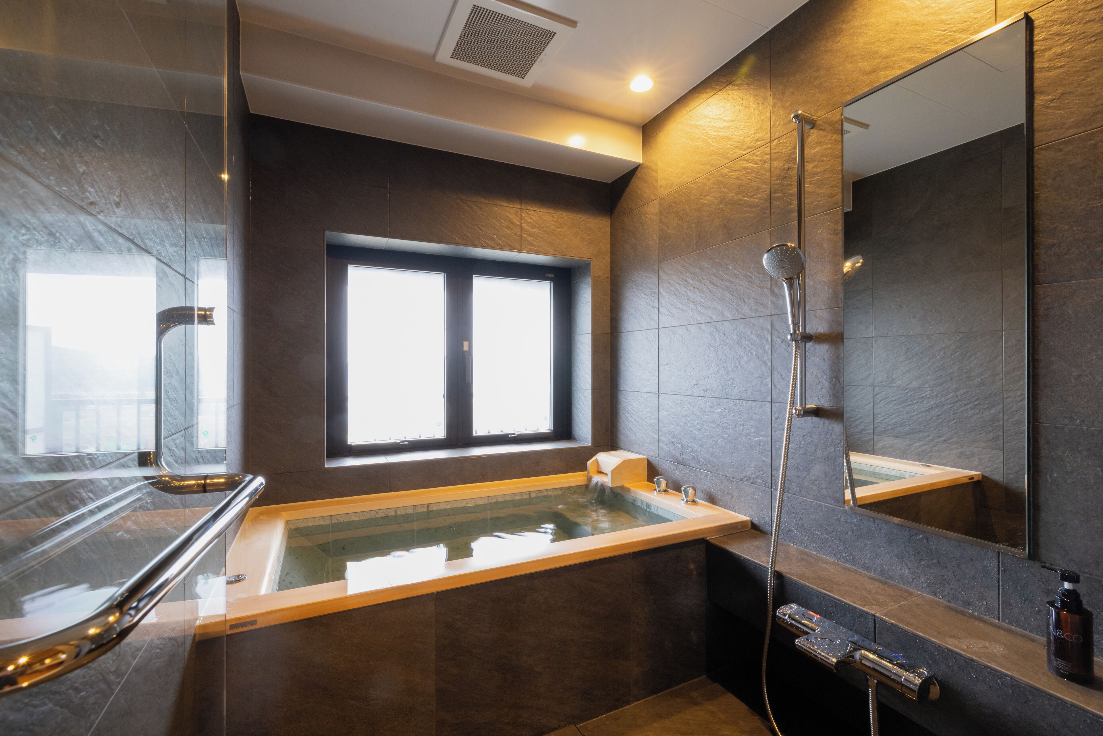 Un baño moderno con una bañera grande, ducha y ventana que deja entrar luz natural.