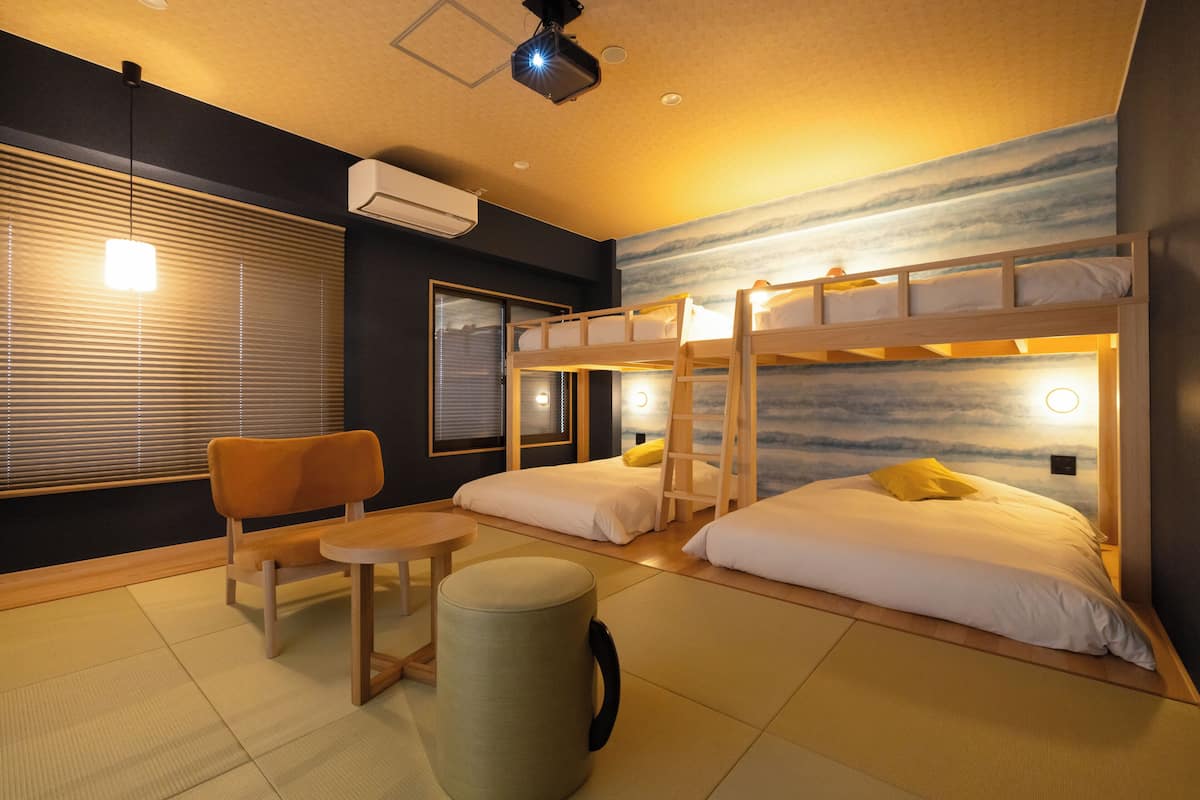 Une chambre d’hôtel avec des lits superposés, une petite table, une chaise et un sol recouvert de tatamis.