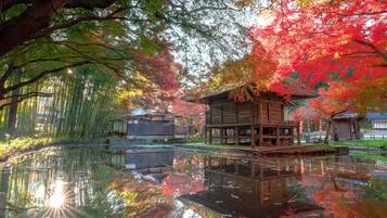 A traditional wooden structure by a reflective water body, surrounded by trees with autumn foliage.