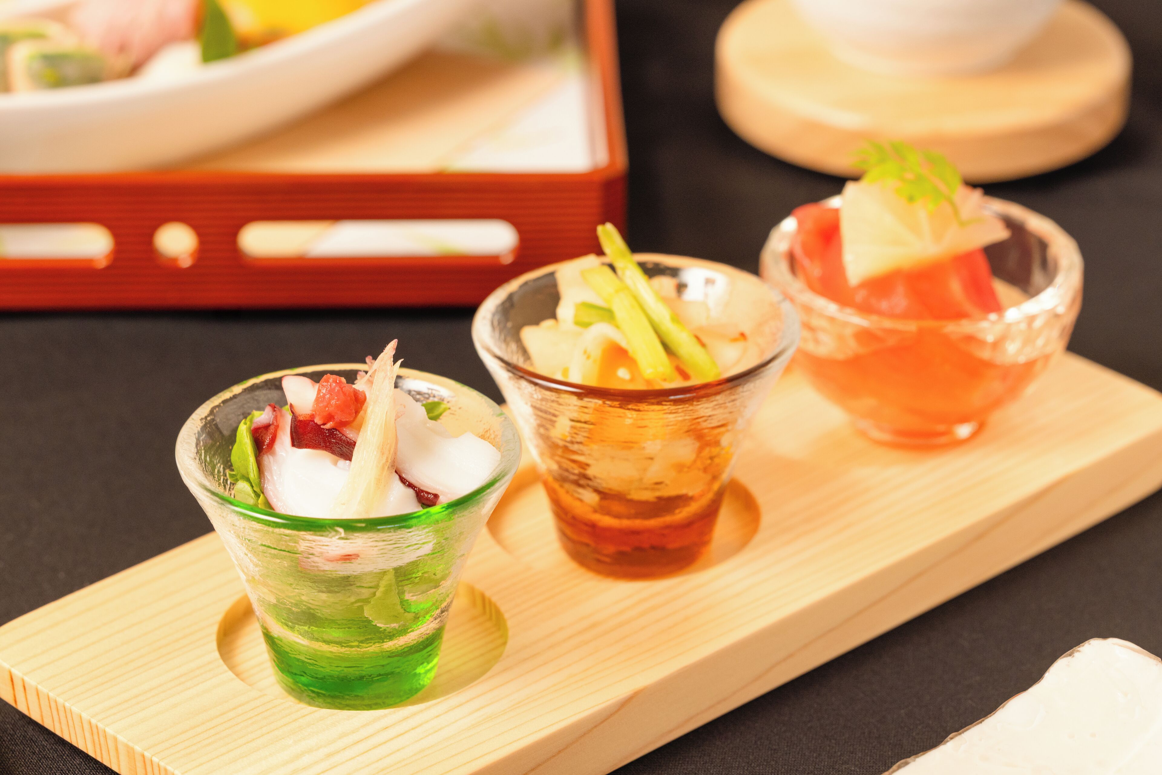 Three small glass dishes with various food items on a wooden tray.
