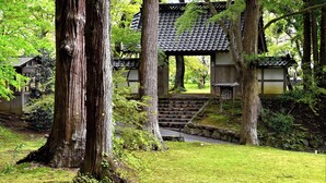 A traditional Japanese building with a tiled roof, surrounded by large trees and a stone pathway leading to the entrance. - ITSUMU (Oshu)