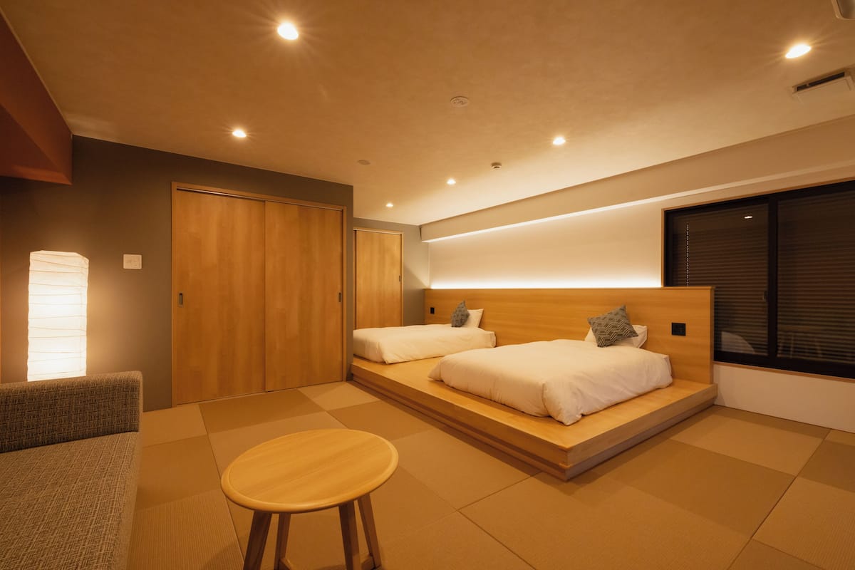 Une chambre moderne avec deux lits, une tête de lit en bois, une petite table ronde et une porte coulissante.
