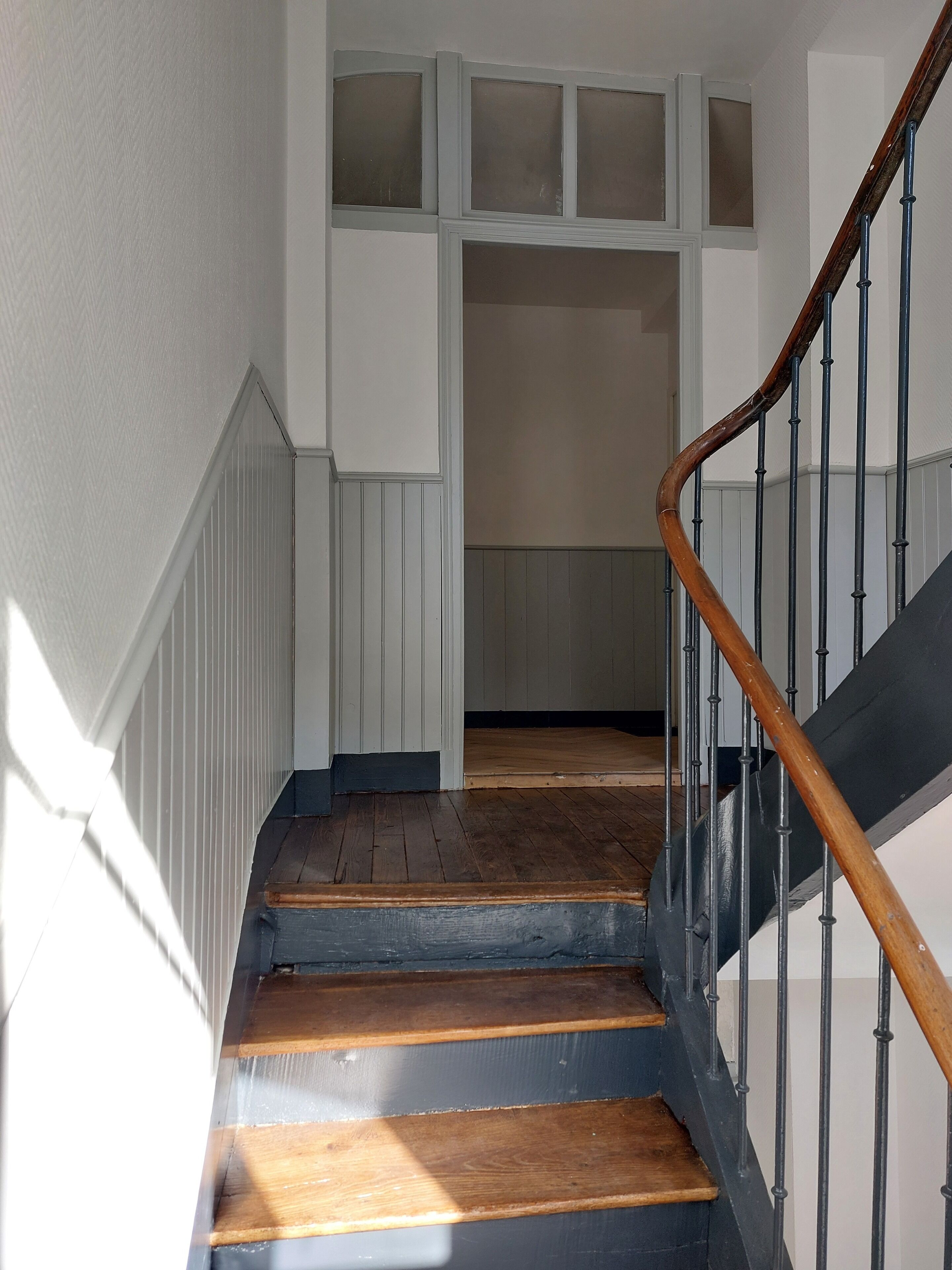A staircase with wooden steps and a metal railing, leading to a landing with a white door and a window above.