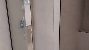 A glass-enclosed shower with a handheld showerhead and a handheld soap dispenser.