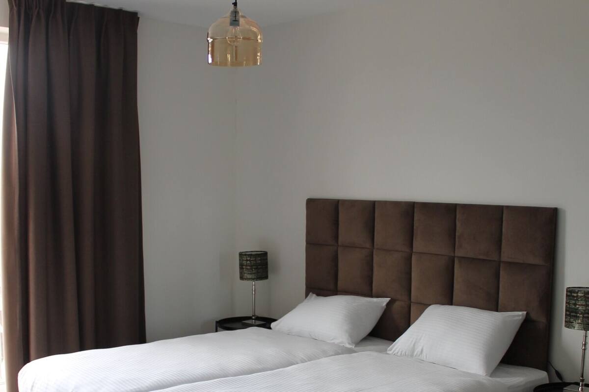A double bed with a tufted headboard, two bedside tables with lamps, and a hanging light fixture.
