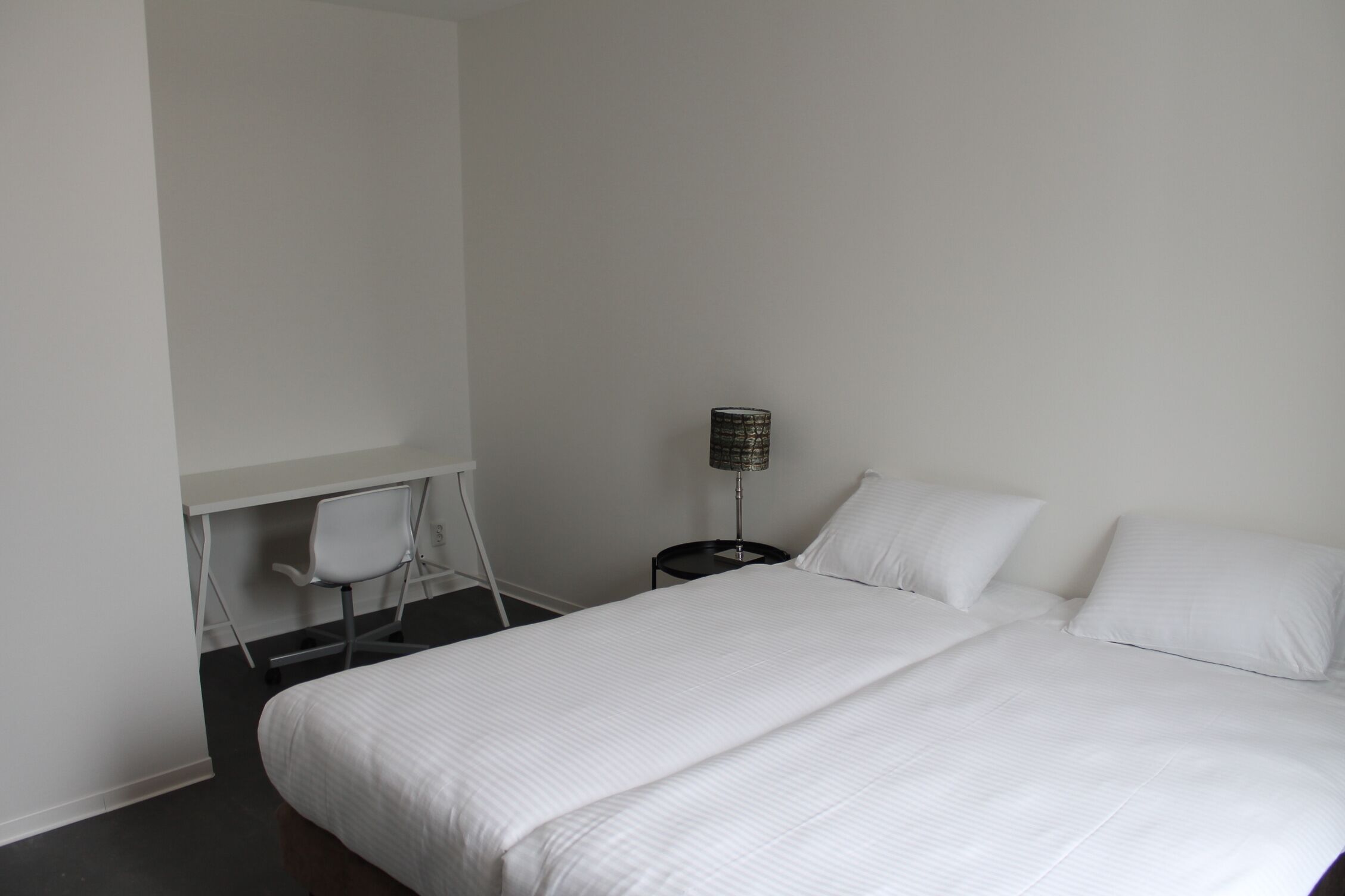 Una habitación de hotel con una cama grande, un escritorio con una silla y una lámpara.