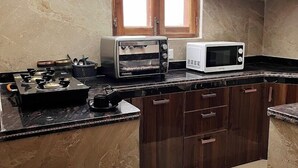 A kitchen with a gas stove, a toaster, and a microwave on a marble countertop. - Classic Hills Villa Mussoorie (Mussoorie)