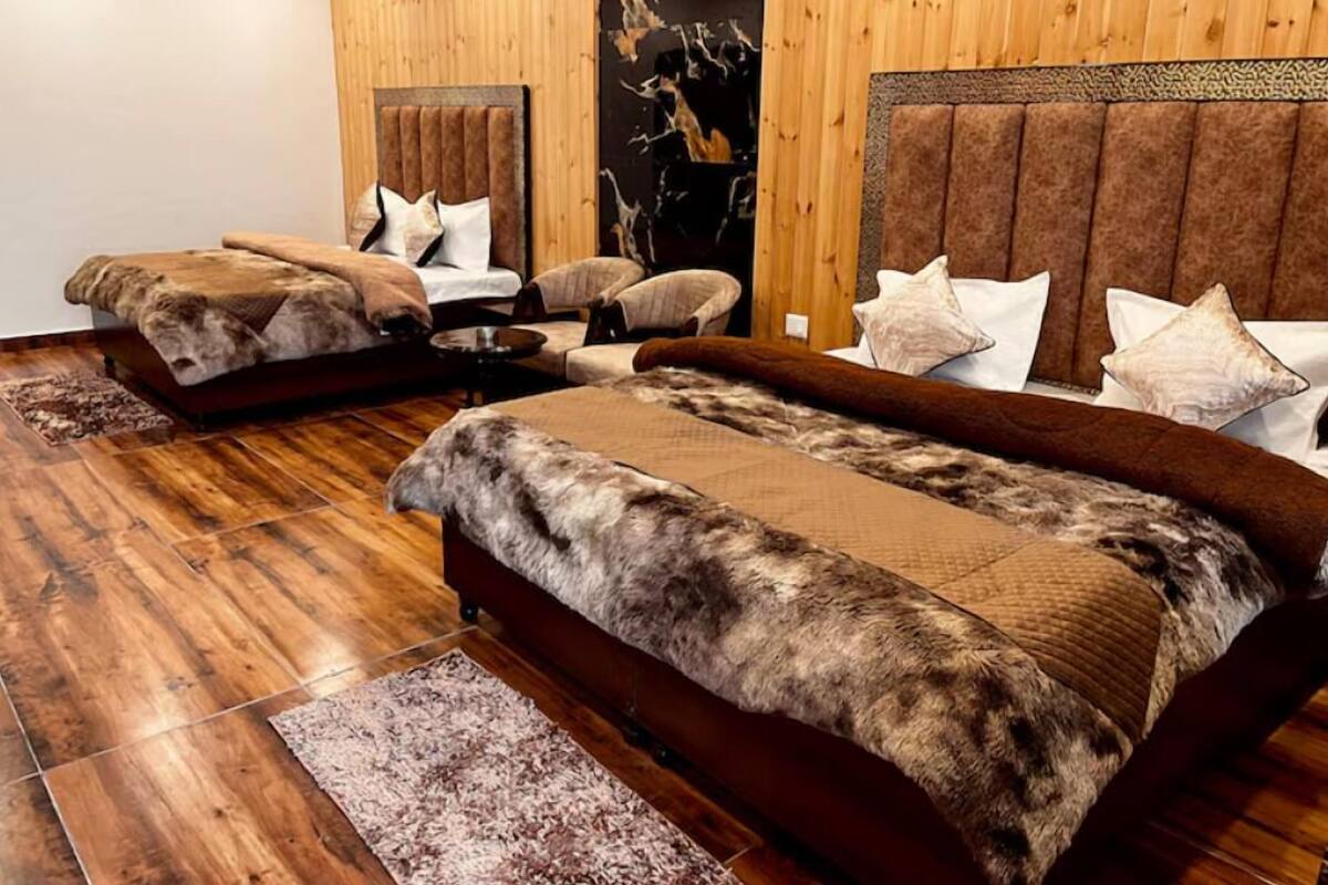 Una habitación con tres camas, cada una con un cubrecolor tipo piel, suelos de madera y una pared de mármol.