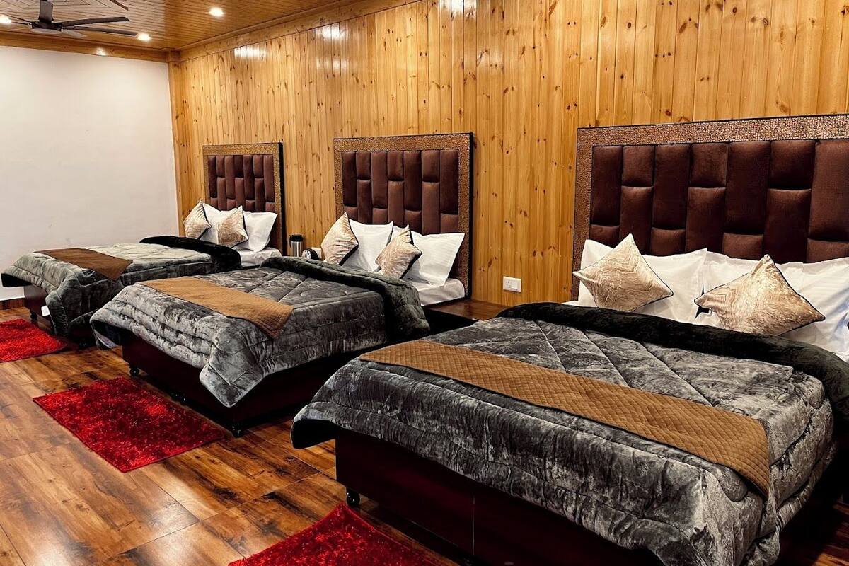Habitación de hotel con tres camas, paredes de madera y una alfombra roja.