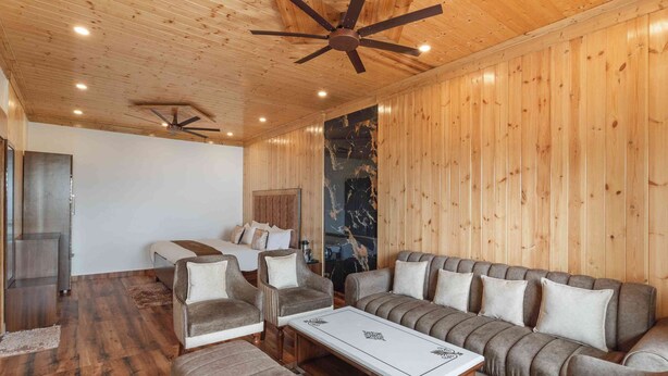 A room with wooden walls, a ceiling fan, a sofa set, a coffee table, and a television. - Classic Hills Villa Mussoorie (Mussoorie)
