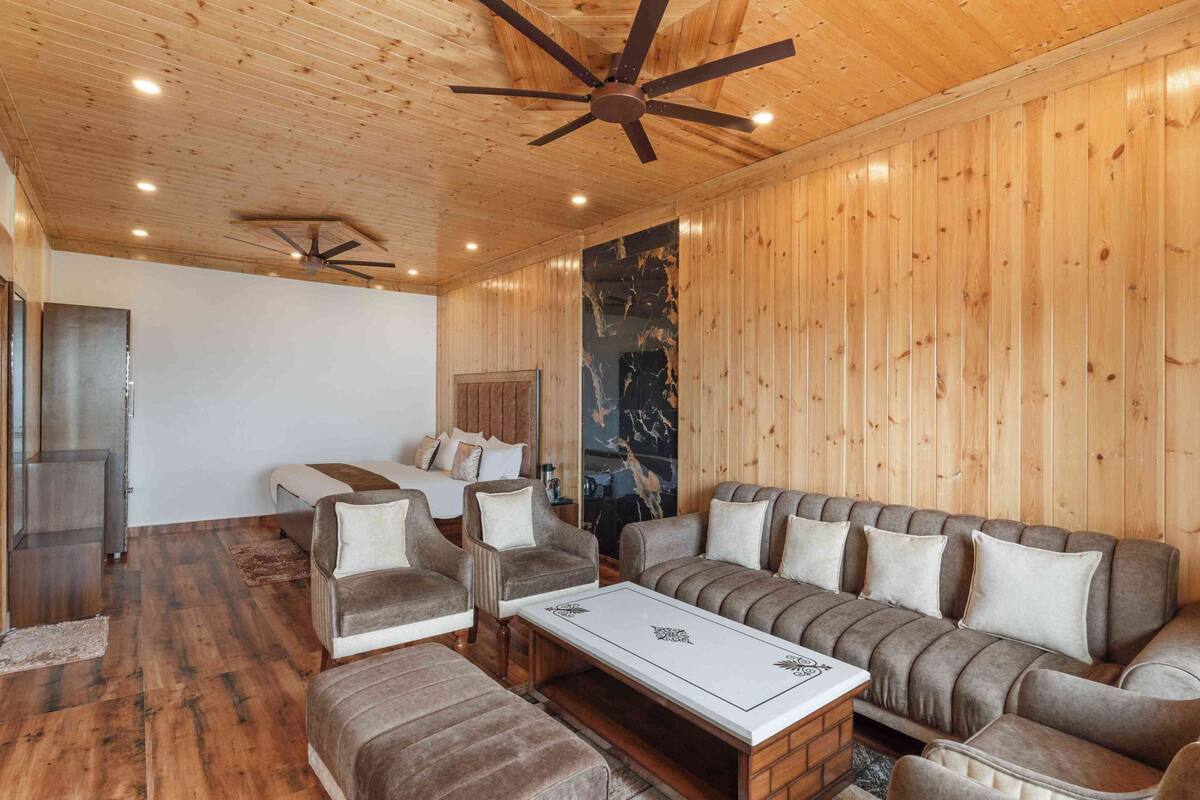 Una habitación con paredes de madera, ventilador de techo, un conjunto de sofás, una mesa de centro y un televisor.