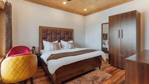 A bedroom with a wooden ceiling, a bed with a headboard, a wardrobe, and a chair. - Classic Hills Villa Mussoorie (Mussoorie)