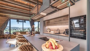 A modern kitchen with a built-in oven and coffee machine, a wooden dining table with a fruit bowl, and a large window overlooking a scenic landscape. - Cozy home in Ravna Gora with sauna (Ravna Gora)