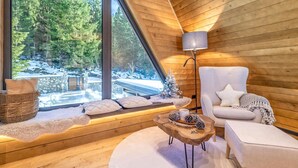 A cozy cabin interior with a large window overlooking a snowy forest, a comfortable chair, a small wooden table, and a lamp. - Cozy home in Ravna Gora with sauna (Ravna Gora)
