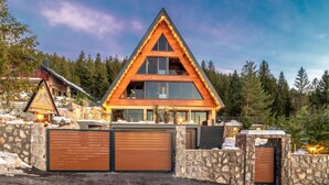 A modern, triangular-shaped lodge with large windows and a stone facade, surrounded by a forested area. - Cozy home in Ravna Gora with sauna (Ravna Gora)