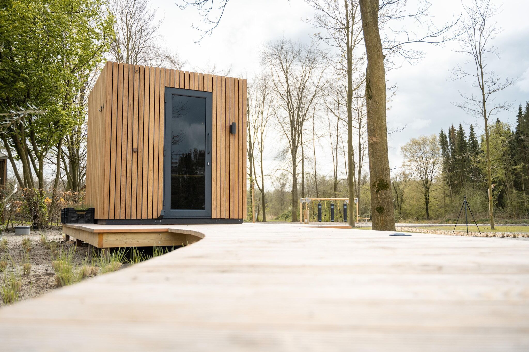 Een moderne houten hut met een grote glazen deur, gelegen op een houten terras, omgeven door bomen.