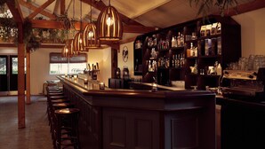 A bar area with a wooden bar counter, hanging pendant lights, and a variety of bottles and glasses on shelves. - Glamping Tent in Zeewolde with BBQ (Zeewolde)