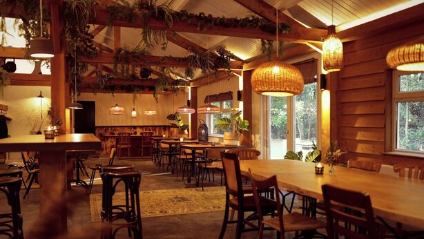 A cozy restaurant with wooden tables and chairs, hanging plants, and warm lighting. - Glamping Tent in Zeewolde with BBQ (Zeewolde)