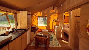 A cozy cabin interior with wooden walls, a kitchen area with a sink and counter, a small dining table, and a bed with a view of the outdoors. - Glamping Tent in Zeewolde with BBQ (Zeewolde)