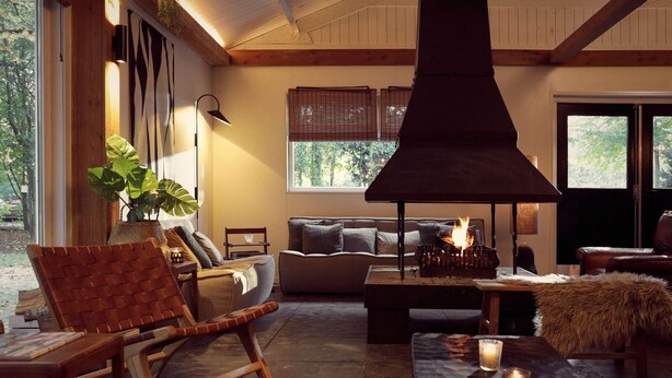 Una sala de estar acogedora con chimenea, asientos cómodos y un amplio ventanal con vistas a la vegetación.