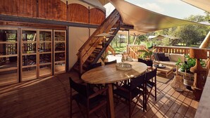 Una terraza de madera con una mesa redonda y sillas, una escalera y un paraguas grande que proporciona sombra.