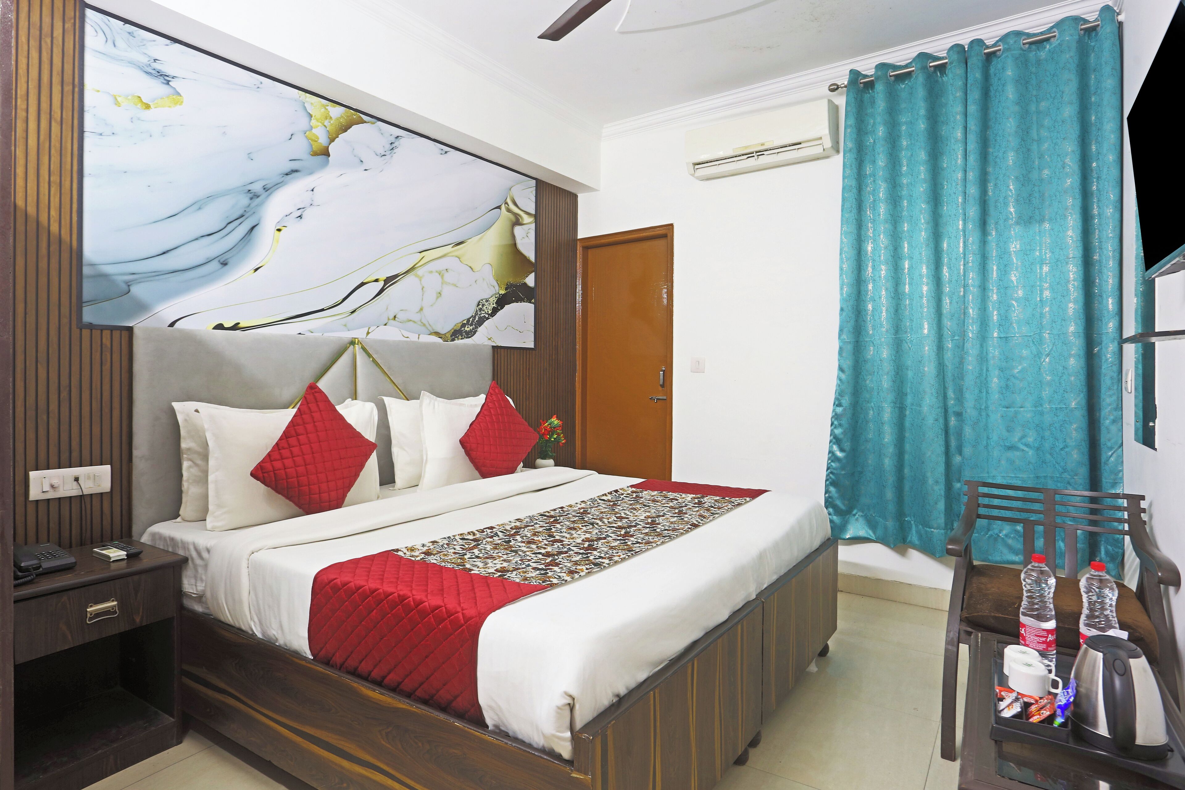 A neatly made bed with a red and white quilt, a wooden nightstand with a phone, and a wall art piece.