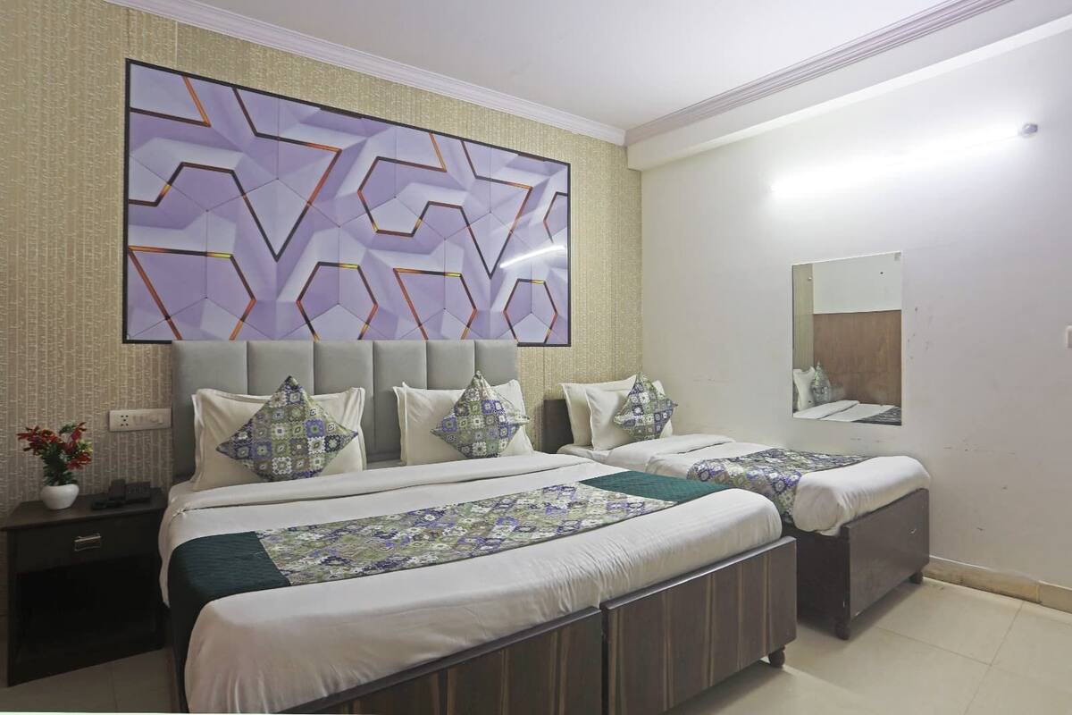 A double bed with a patterned bedspread, a headboard, and decorative pillows. There is a nightstand with a phone and a plant.