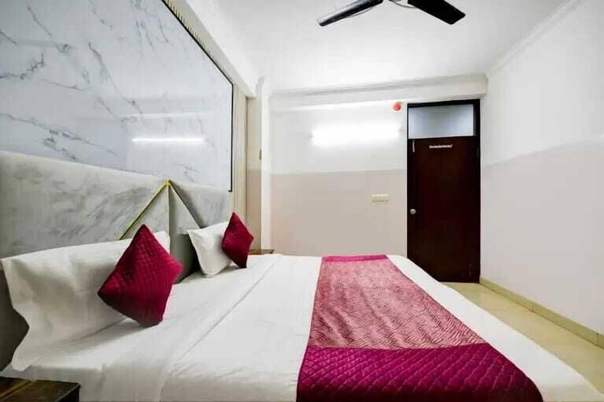 A hotel room with a bed, a ceiling fan, a marble wall, and a door.