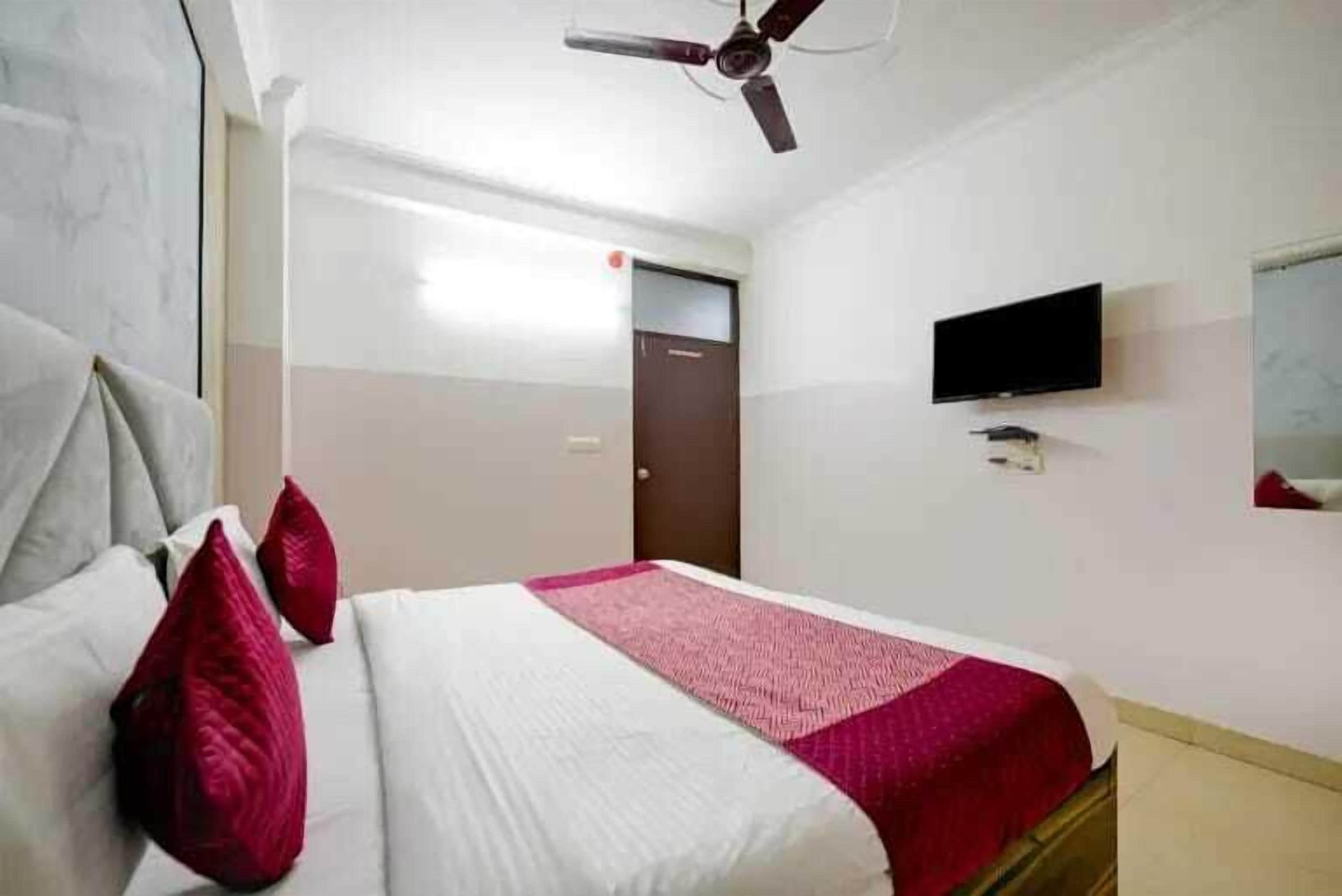 A hotel room with a bed, pillows, a ceiling fan, a TV, and a door.