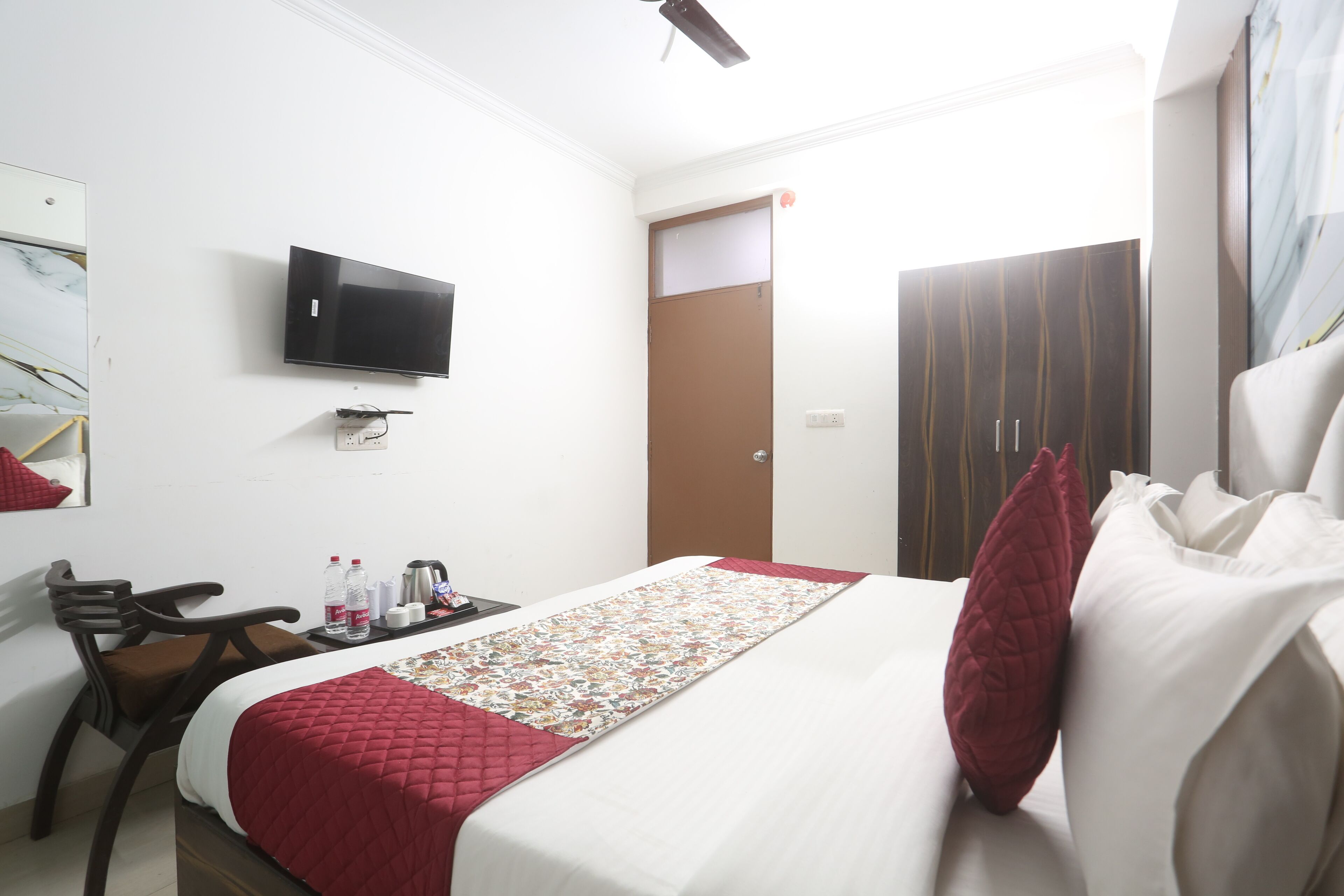 Ein Hotelzimmer mit einem Bett, einem an der Wand befestigten Fernseher, einem Schreibtisch mit Stuhl und einer Tür.