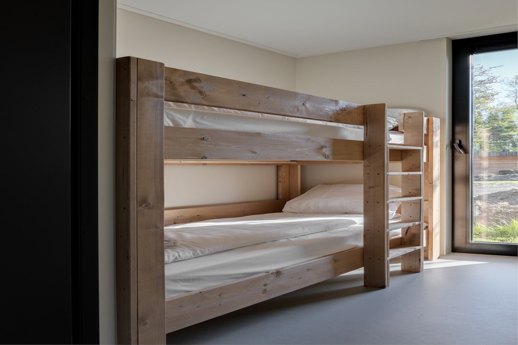 A bunk bed with a wooden frame and white bedding in a room with a large window.