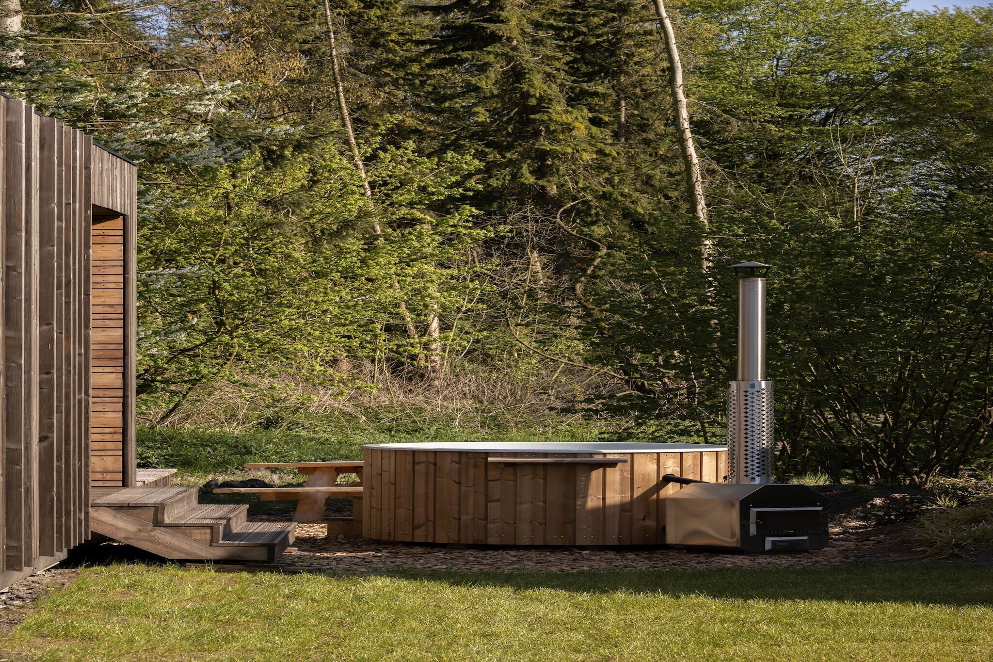 A wooden cabin with a hot tub and a chimney, surrounded by trees.