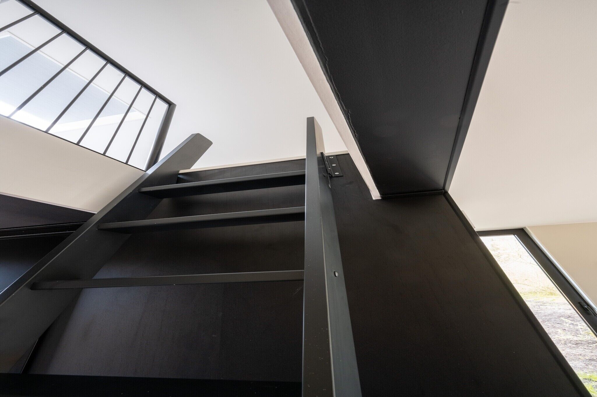 Ein modernes Interieur mit einer dunklen Treppe und einem Fenster mit Metallgeländer.