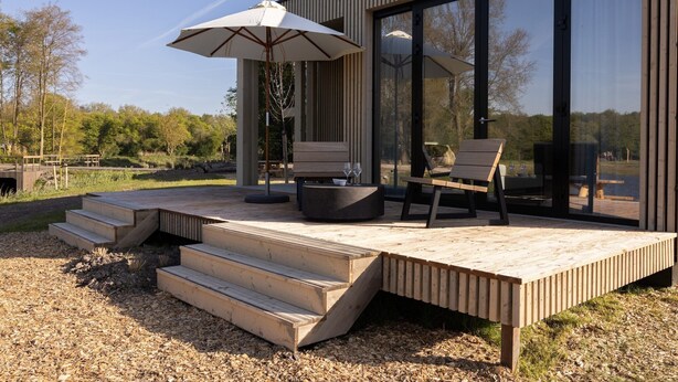 Una terraza moderna al aire libre con escalones de madera, una mesa redonda, dos sillas y un paraguas grande.