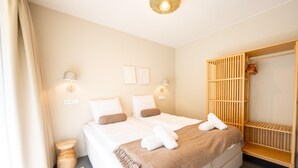 A neatly made bed with white linens and a brown throw blanket, a wooden wardrobe, and two wall-mounted light fixtures. - Water Lodge in Lelystad with Private Sauna (Zeewolde)
