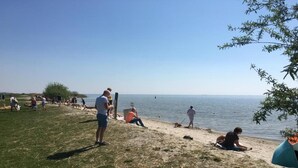 A beach with people relaxing, a tent, and a clear sky. - Water Lodge in Lelystad with Private Sauna (Zeewolde)