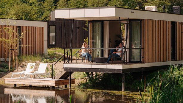 A modern houseboat with a deck, two people sitting, and a small garden area. - Water Lodge in Lelystad with Private Sauna (Zeewolde)