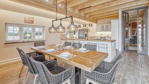 A spacious dining area with a wooden table and wicker chairs, a kitchen with white cabinets, and a view of the outdoors through large windows. - 3 bedroom stunning home in Sittensen Kalbe (Sittensen Kalbe)