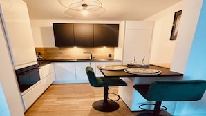 Une cuisine compacte avec des meubles de couleur sombre, un plan de travail en bois et deux tabourets de bar verts.